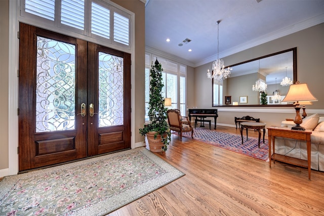 foyer with light hardwood / wood-style flooring, french doors, ornamental molding, and a chandelier