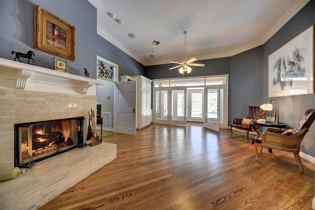 living room featuring french doors, a tile fireplace, hardwood / wood-style floors, crown molding, and ceiling fan