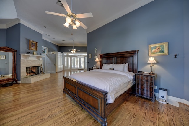 bedroom featuring ornamental molding, light hardwood / wood-style flooring, a multi sided fireplace, and ceiling fan