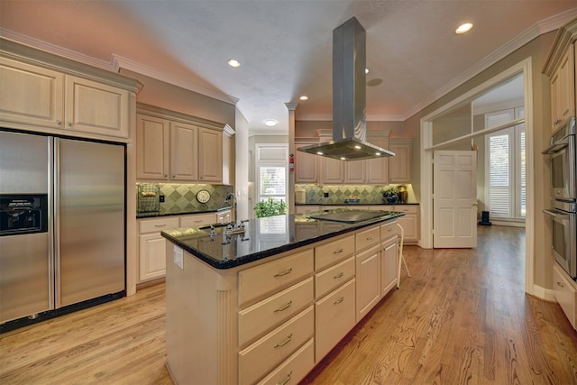 kitchen with appliances with stainless steel finishes, light wood-type flooring, island range hood, ornamental molding, and a center island with sink