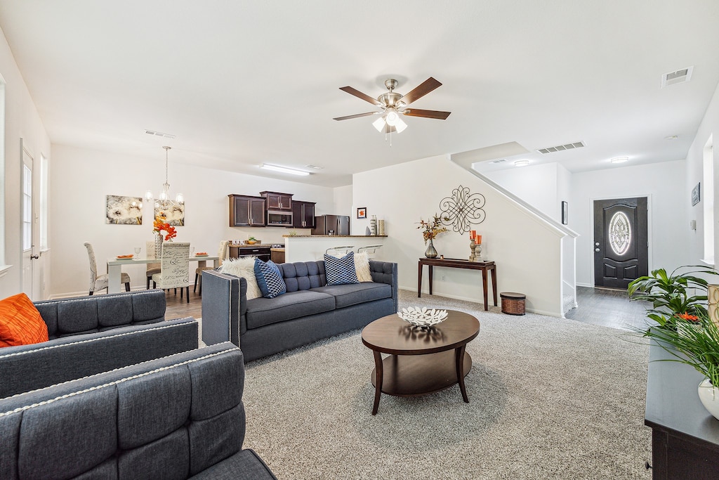 living room featuring light colored carpet and ceiling fan with notable chandelier