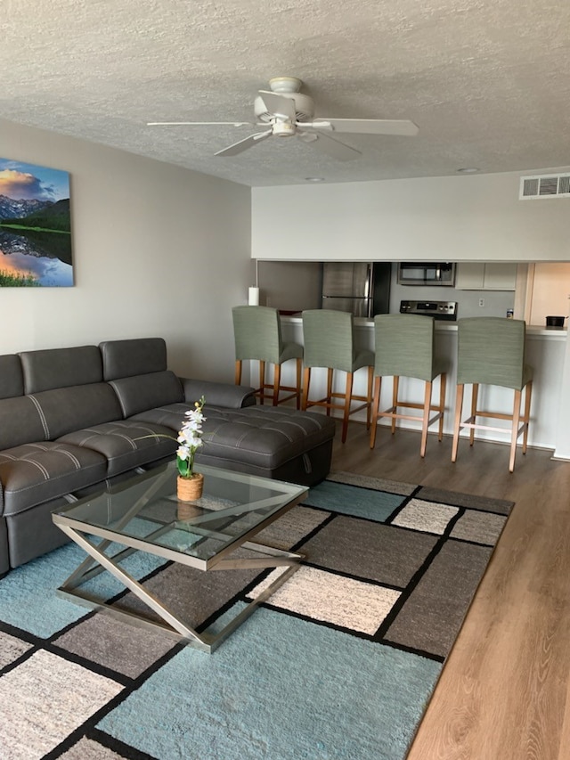 living room with a textured ceiling, wood-type flooring, and ceiling fan