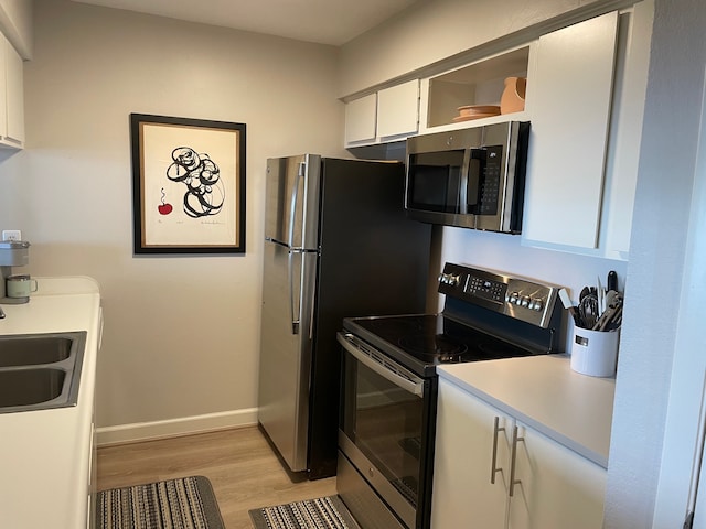 kitchen with sink, white cabinetry, stainless steel appliances, and light hardwood / wood-style floors