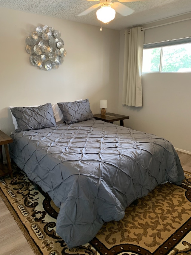 bedroom featuring ceiling fan, hardwood / wood-style flooring, and a textured ceiling