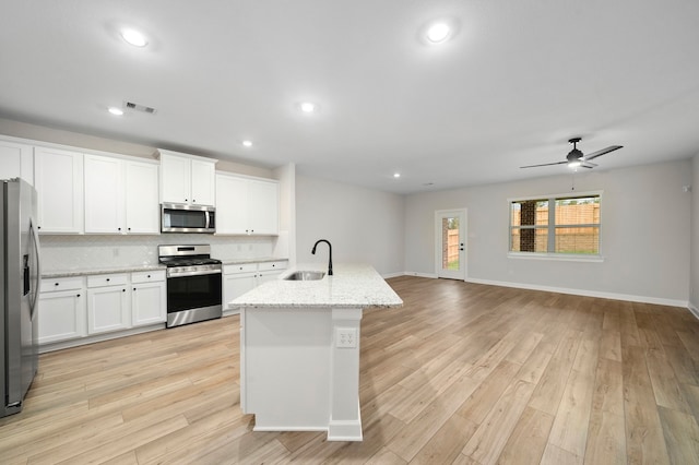 kitchen featuring a center island with sink, appliances with stainless steel finishes, white cabinets, and light hardwood / wood-style floors