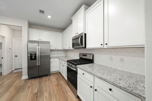 kitchen with decorative backsplash, white cabinets, light stone counters, light hardwood / wood-style floors, and stainless steel appliances