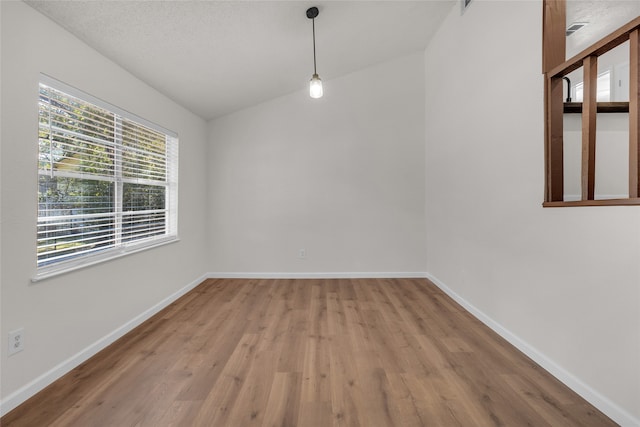 spare room with light hardwood / wood-style flooring, a textured ceiling, and lofted ceiling