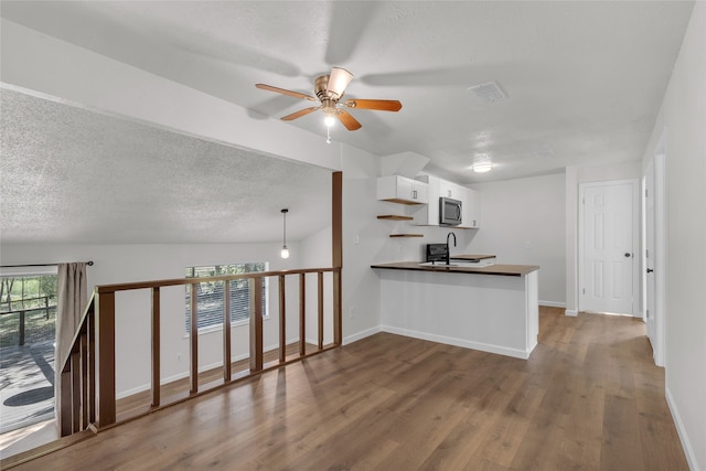 kitchen with sink, kitchen peninsula, hanging light fixtures, white cabinetry, and hardwood / wood-style flooring