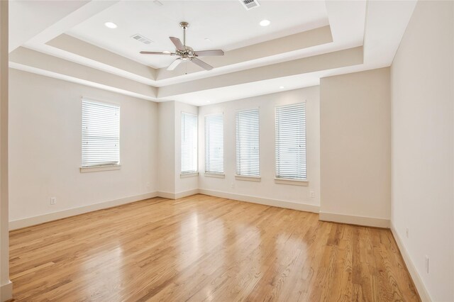 empty room with a tray ceiling, ceiling fan, and light hardwood / wood-style floors