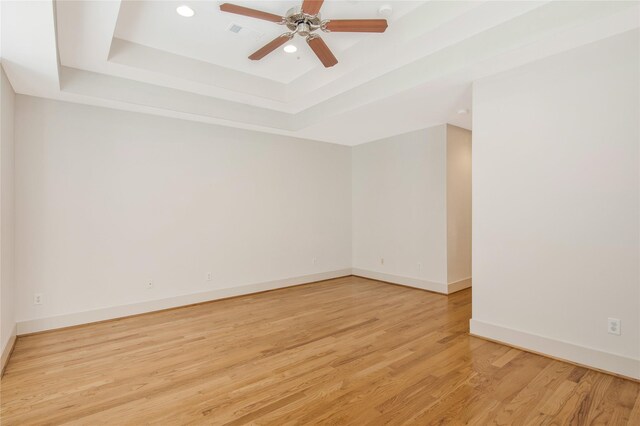 empty room with ceiling fan, light hardwood / wood-style floors, and a raised ceiling