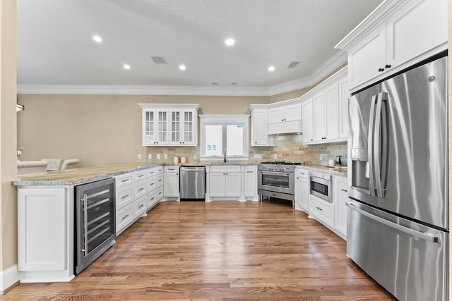 kitchen featuring white cabinetry, appliances with stainless steel finishes, kitchen peninsula, beverage cooler, and light stone countertops