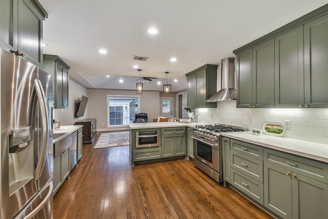 kitchen featuring pendant lighting, green cabinets, kitchen peninsula, stainless steel appliances, and wall chimney range hood