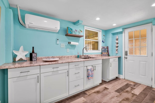 kitchen with white cabinetry, a wealth of natural light, an AC wall unit, light hardwood / wood-style floors, and sink