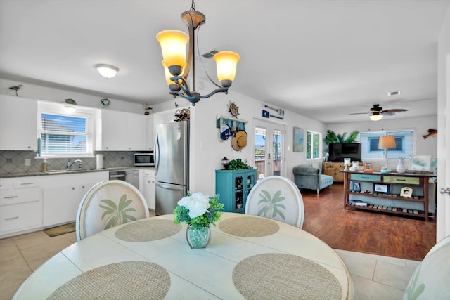 dining space featuring french doors, ceiling fan with notable chandelier, light wood-type flooring, and a healthy amount of sunlight