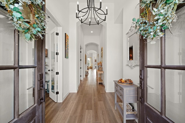 hallway featuring french doors, a high ceiling, light wood-type flooring, and an inviting chandelier