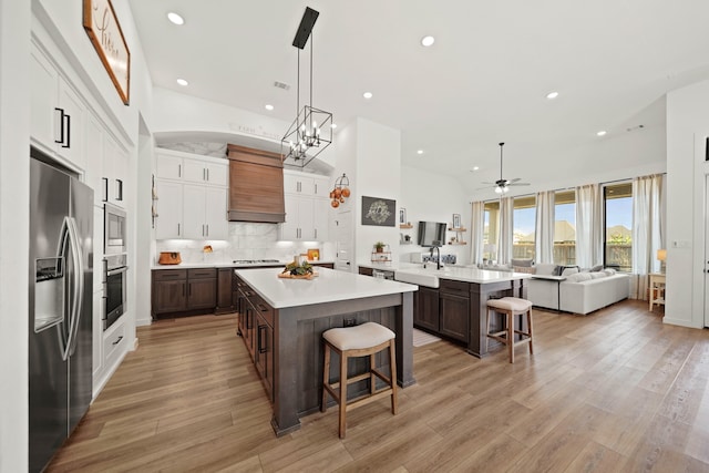 kitchen featuring a breakfast bar, appliances with stainless steel finishes, custom range hood, and light hardwood / wood-style floors