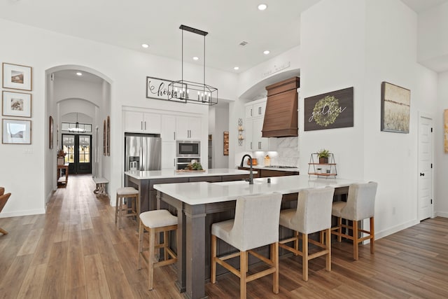 kitchen with backsplash, white cabinetry, custom exhaust hood, hardwood / wood-style flooring, and a breakfast bar