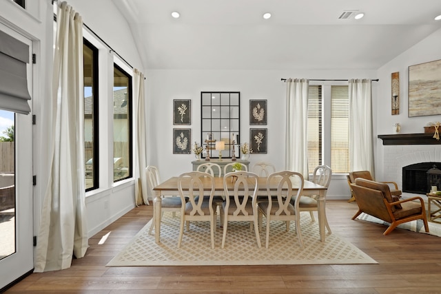 dining space featuring vaulted ceiling, a brick fireplace, and light hardwood / wood-style floors