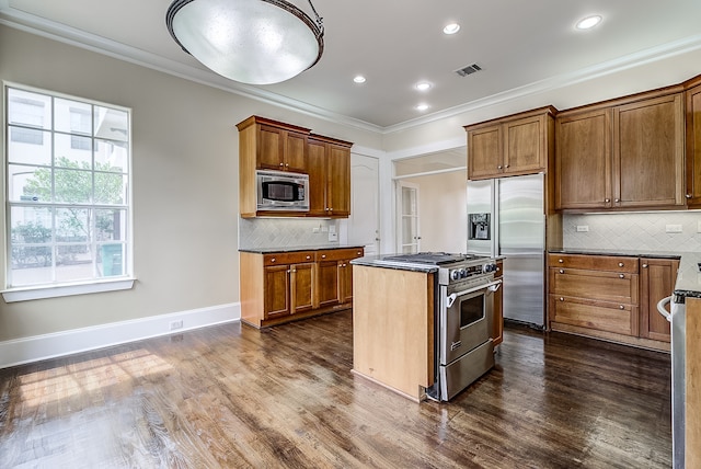 kitchen with tasteful backsplash, dark hardwood / wood-style flooring, appliances with stainless steel finishes, ornamental molding, and a center island