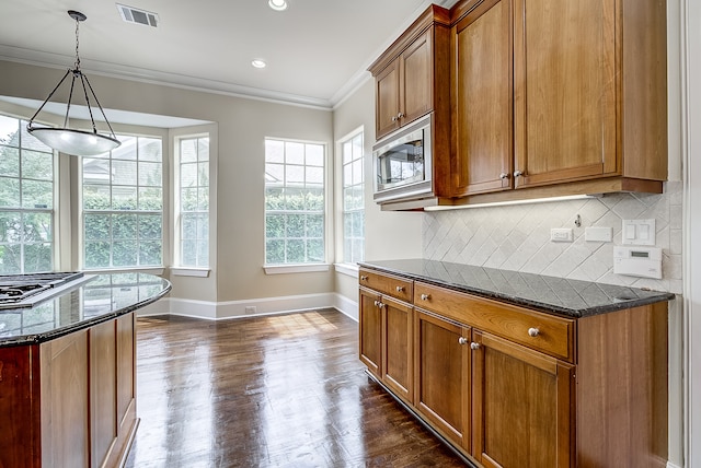 kitchen with dark hardwood / wood-style flooring, appliances with stainless steel finishes, dark stone counters, ornamental molding, and decorative light fixtures