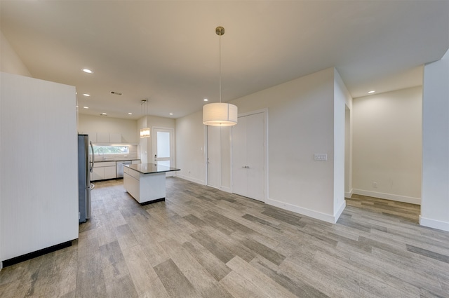 kitchen featuring hanging light fixtures, a kitchen island, white cabinetry, stainless steel refrigerator, and light hardwood / wood-style flooring