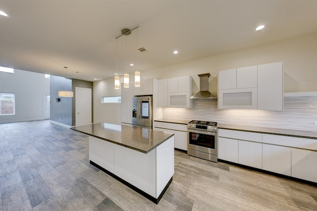 kitchen featuring hanging light fixtures, stainless steel appliances, wall chimney exhaust hood, and white cabinets