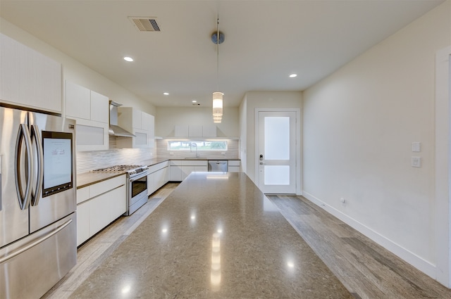 kitchen with wall chimney range hood, stainless steel appliances, decorative light fixtures, white cabinets, and light hardwood / wood-style floors