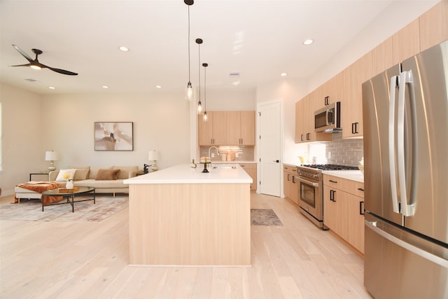 kitchen featuring hanging light fixtures, a kitchen island with sink, light brown cabinetry, light hardwood / wood-style floors, and stainless steel appliances