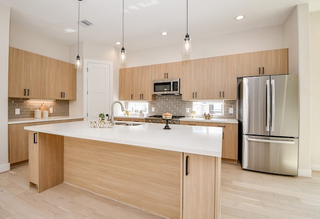 kitchen with light brown cabinets, a center island with sink, light hardwood / wood-style flooring, sink, and stainless steel appliances