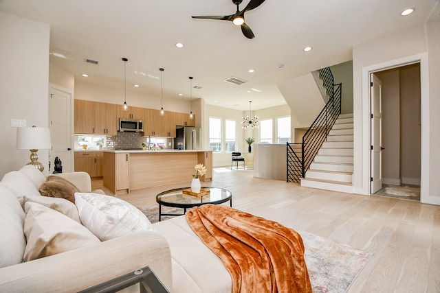 living room featuring light wood-type flooring and ceiling fan with notable chandelier