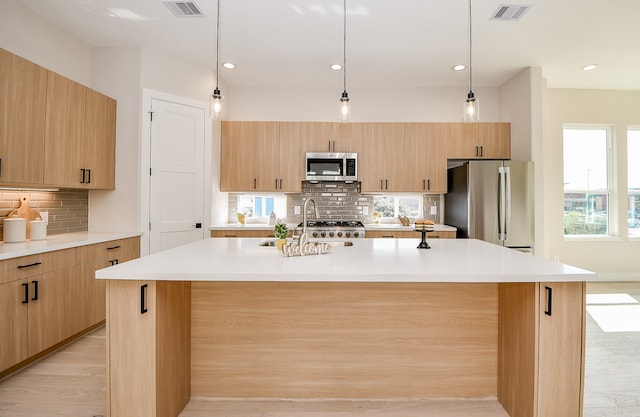 kitchen featuring light brown cabinetry, appliances with stainless steel finishes, light hardwood / wood-style flooring, and an island with sink