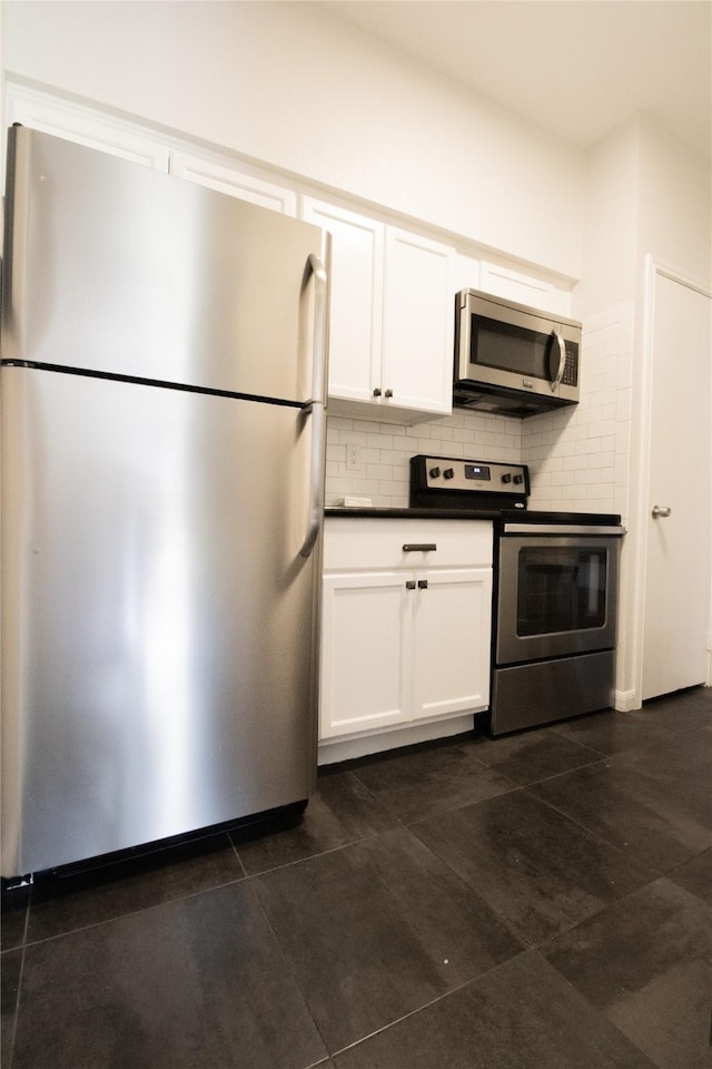 kitchen featuring tasteful backsplash, white cabinets, dark tile patterned flooring, and stainless steel appliances