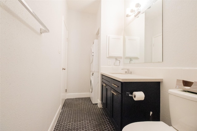 bathroom featuring stacked washing maching and dryer, toilet, and vanity