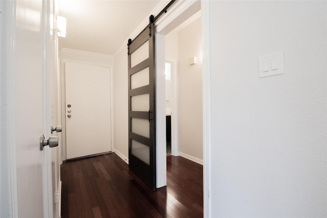 corridor with a barn door, dark hardwood / wood-style floors, and ornamental molding