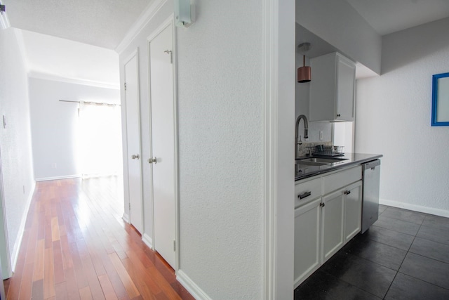 corridor featuring dark wood finished floors, baseboards, a textured wall, and a sink