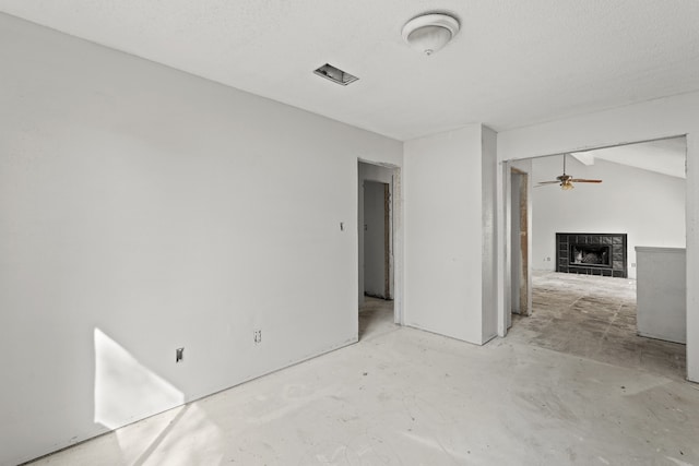 spare room with a textured ceiling, a tiled fireplace, ceiling fan, and vaulted ceiling