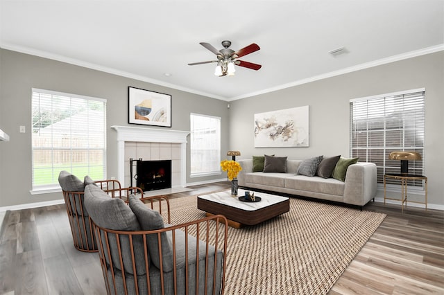 living room featuring ceiling fan, wood-type flooring, a tile fireplace, and crown molding