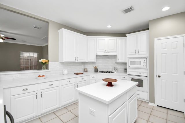 kitchen with light tile patterned flooring, tasteful backsplash, white appliances, a center island, and white cabinets