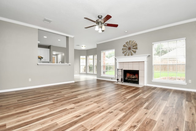 unfurnished living room featuring light hardwood / wood-style floors, crown molding, a tile fireplace, and a wealth of natural light