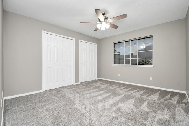 unfurnished bedroom featuring ceiling fan, carpet flooring, and two closets