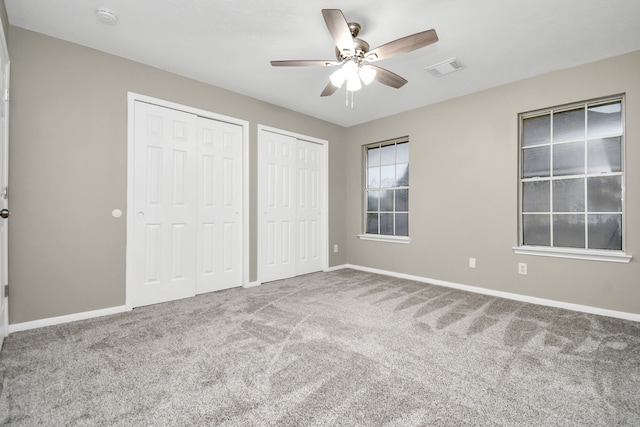 unfurnished bedroom featuring carpet, multiple closets, and ceiling fan