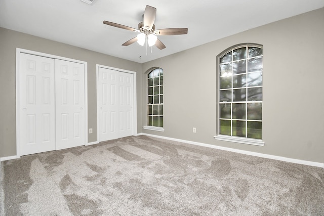 unfurnished bedroom featuring multiple closets, carpet flooring, and ceiling fan