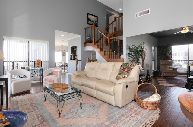 living room with ceiling fan, a towering ceiling, and hardwood / wood-style floors