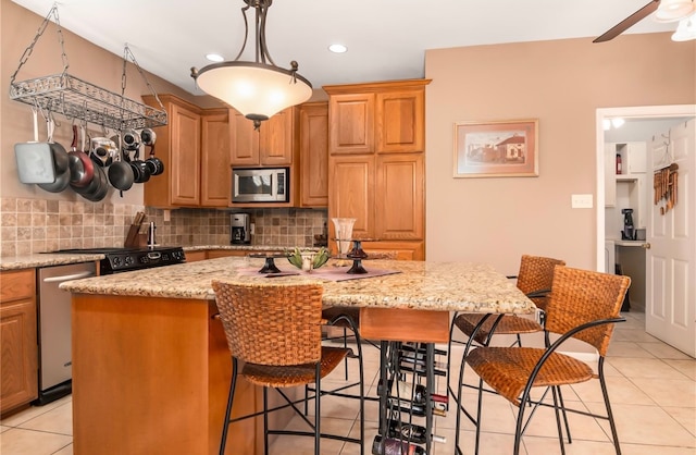 kitchen featuring light stone countertops, a center island, light tile patterned flooring, appliances with stainless steel finishes, and tasteful backsplash