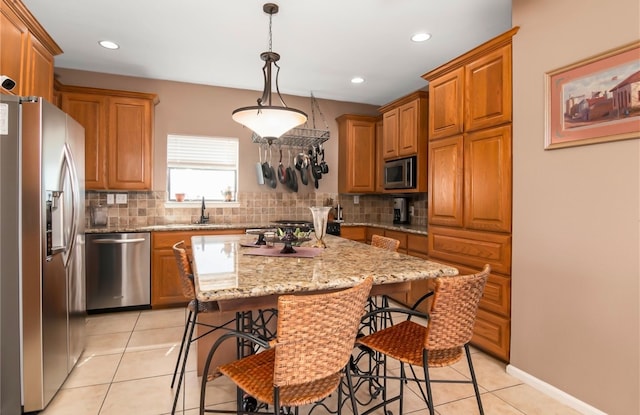 kitchen with appliances with stainless steel finishes, light stone countertops, light tile patterned flooring, pendant lighting, and a center island