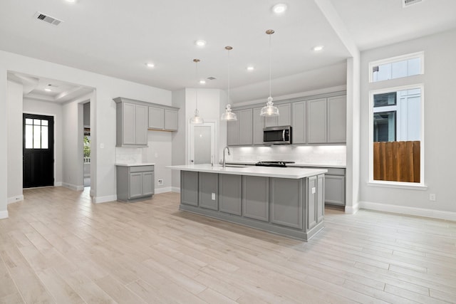 kitchen with gray cabinets, light hardwood / wood-style floors, a kitchen island with sink, and hanging light fixtures