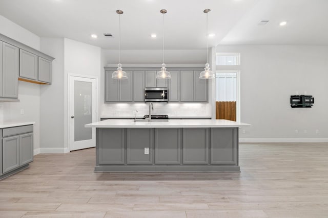 kitchen with decorative light fixtures, a kitchen island with sink, gray cabinetry, and light hardwood / wood-style floors