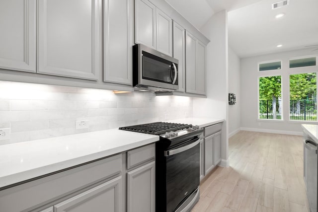 kitchen with decorative backsplash, stainless steel appliances, light hardwood / wood-style floors, and gray cabinetry