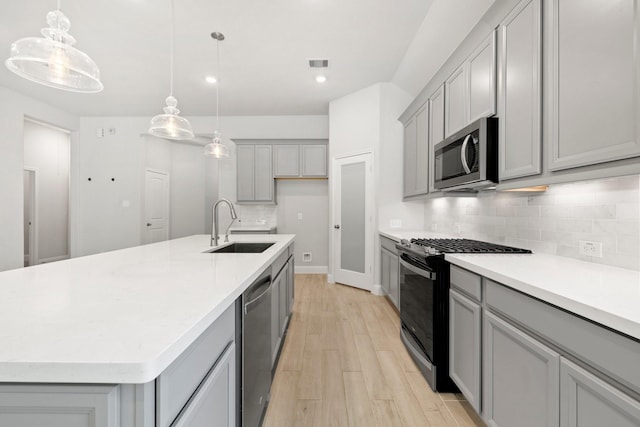 kitchen featuring a center island with sink, sink, light hardwood / wood-style flooring, decorative light fixtures, and stainless steel appliances