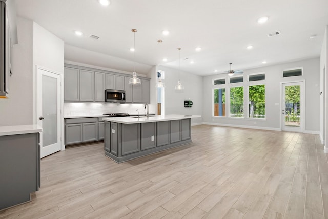 kitchen with gray cabinetry, a kitchen island with sink, sink, ceiling fan, and decorative light fixtures